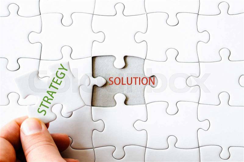 Hand with missing jigsaw puzzle piece. Word STRATEGY, covering text SOLUTION. Business concept image for completing the final puzzle piece, stock photo