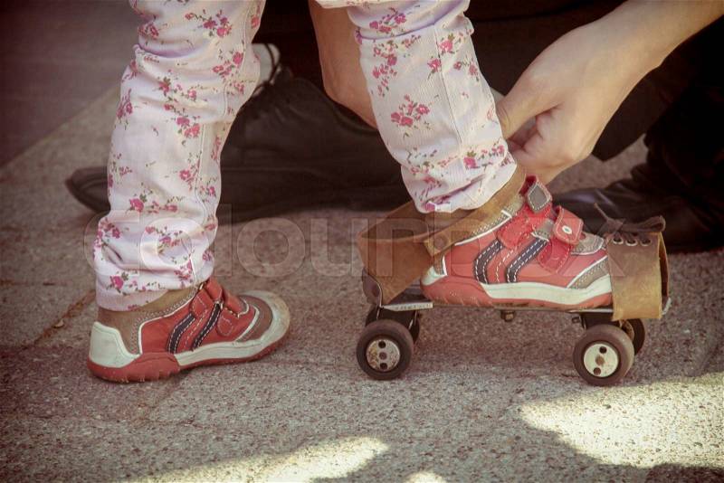 Father helping her little daughter to try on vintage roller skates. Old film photo style, stock photo