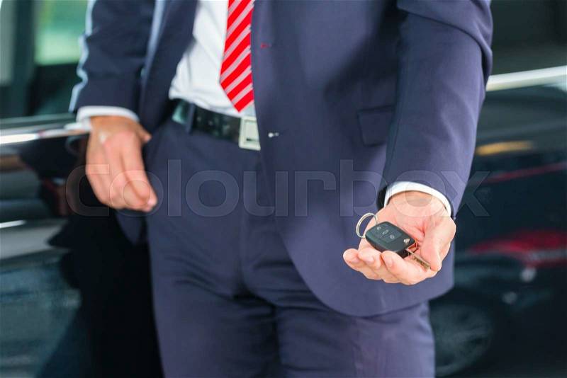 Seller or car salesman in car dealership with key presenting his new and used cars in the showroom, stock photo