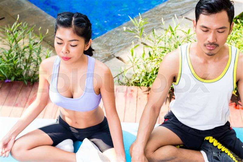 Asian couple in lotus seat at yoga pose exercise in front of tropical pool, stock photo