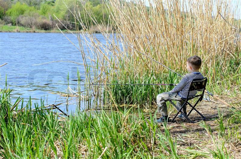 Young Boy Sitting on a Chair at the Riverside, Holding his Fishing Rod While Catching Fish at the River, stock photo