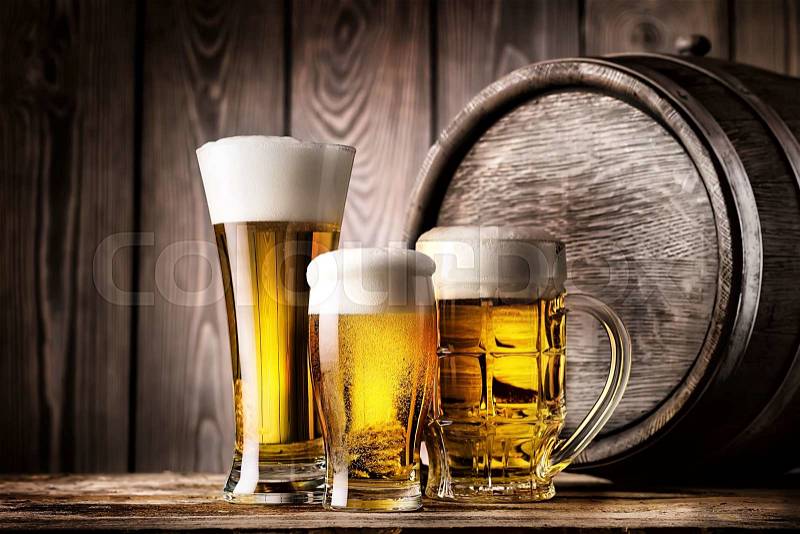 Two glasses and mug of light beer on a background of the old wooden barrels, stock photo