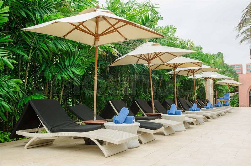 Many chairs and white umbrellas besides swimming pool, stock photo