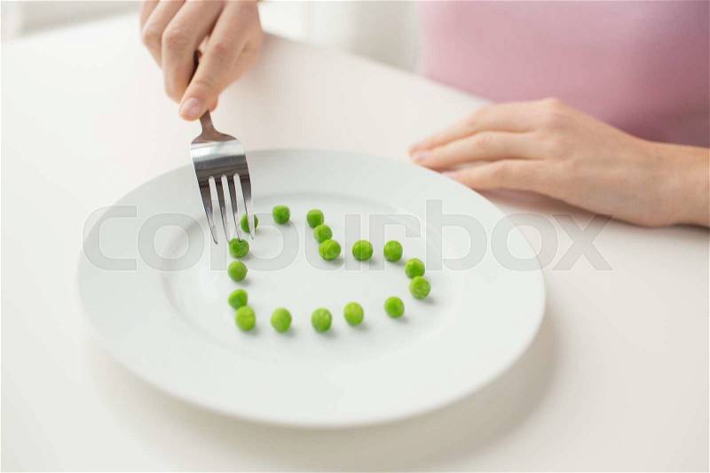 Healthy eating, dieting, vegetarian food and people concept - close up of woman with fork eating peas in shape of heart, stock photo
