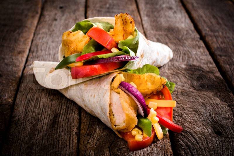 Tortilla wrap sandwich with fried chicken and vegetables on wooden background,selective focus, stock photo