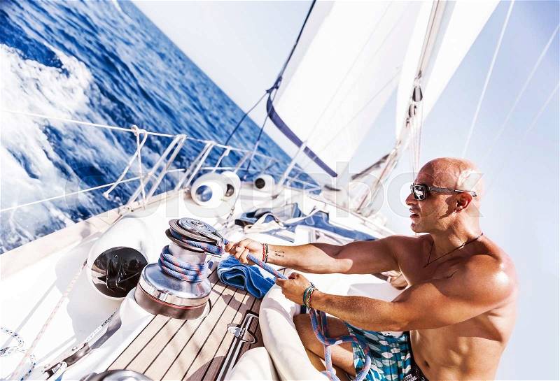 Handsome man working on sailboat, pulling rope, active summer vacation on water transport, having fun in the sea, enjoying water sport, stock photo