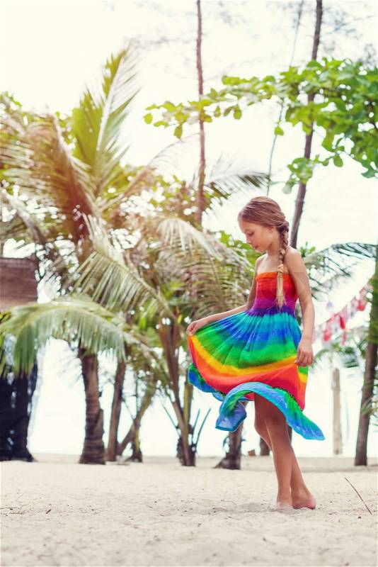 8 years old girl wearing colorful rainbow dress resting on the tropical palm beach in Thailand in summer, stock photo