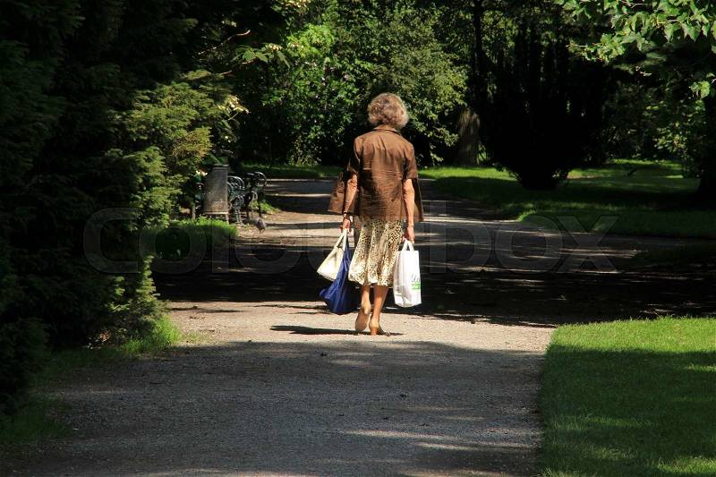 The solitary lady goes to home with her shopping bags and walks through the park in the summer, stock photo