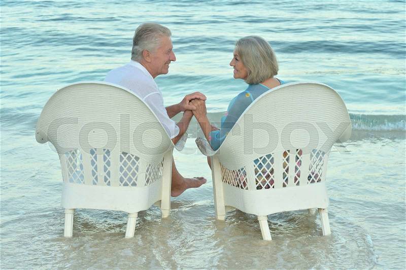 Elderly couple sitting on the shore and looking at each other, stock photo