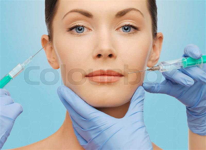 Plastic surgery, injections and beauty concept - beautiful young woman face and surgeon hands with syringes over blue background, stock photo