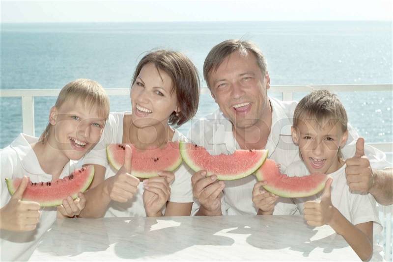 Friendly family eating watermelon in the against the sea in summer, stock photo