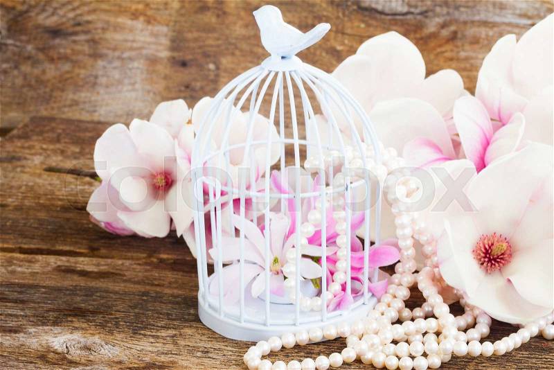 Magnolia fresh flowers with pearls and birdcage on wooden table, stock photo