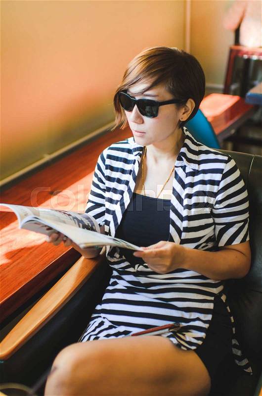 Smart short hair woman wearing sun glasses sitting in the cafe read magazine, stock photo