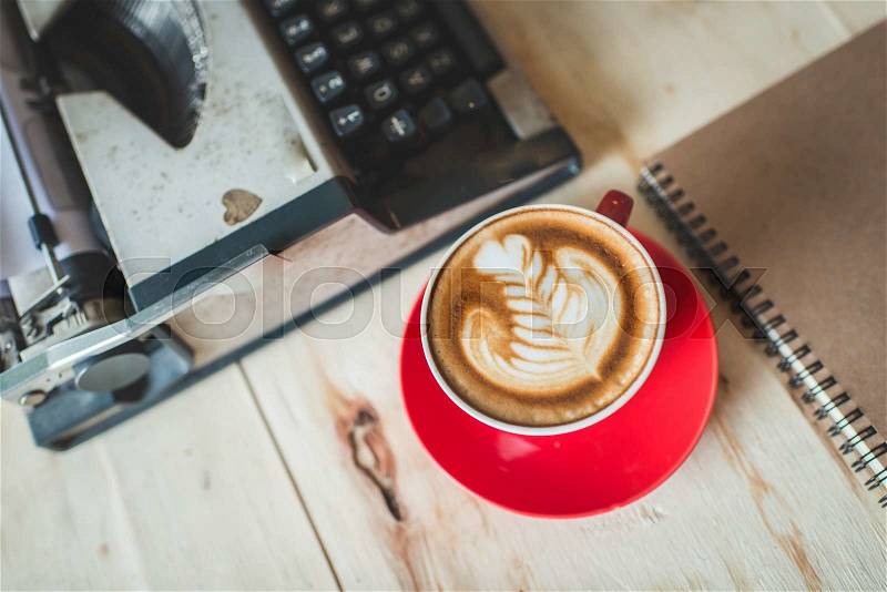 Latte art in red coffee cup and Typewriter on wooden table, stock photo