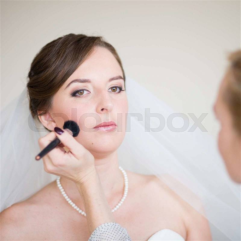 Stylist making up young beautiful bride before wedding, stock photo