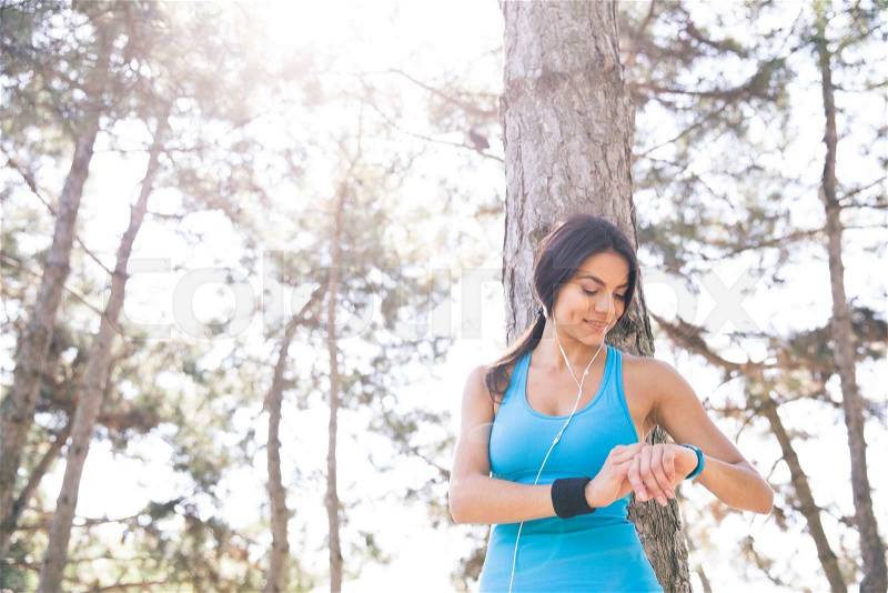 Happy sporty woman using smart watch outdoors in park, stock photo