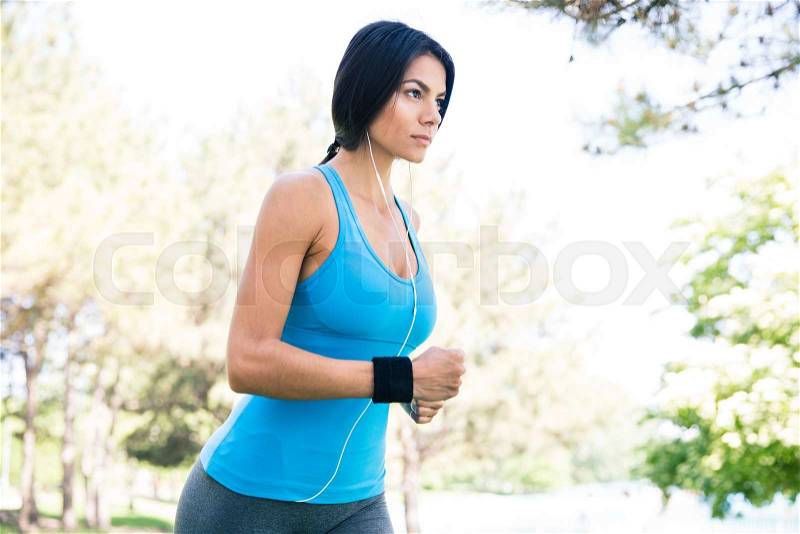 Charming sporty woman in headphones running outdoors in park, stock photo