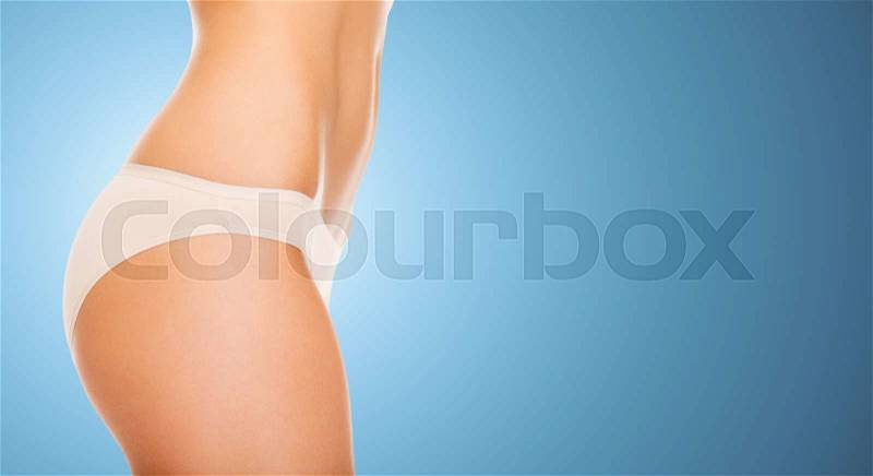 People, health, body care and beauty concept - close up of slim woman tummy and hips in underwear over blue background, stock photo