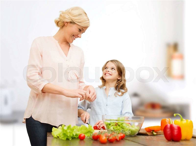 Vegetarian food, culinary, family and people concept - happy mother and daughter cooking vegetable salad for dinner and talking over home kitchen background, stock photo