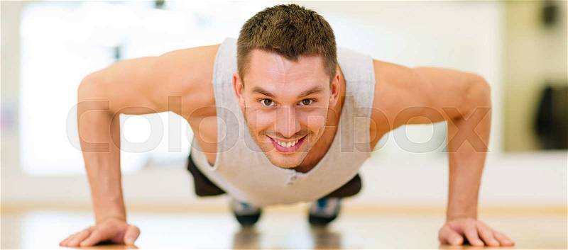 Fitness, sport, training, gym and lifestyle concept - smiling man doing push-ups in the gym, stock photo