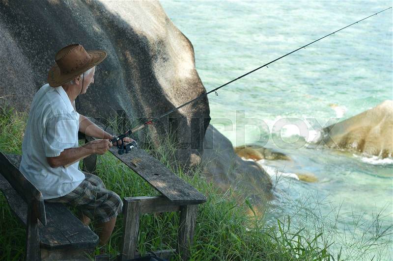 Elderly man fishing in the sea with a fishing rod, stock photo