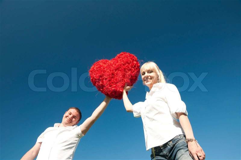 Couple of young people, loving boy and girl holding hands in the heart of roses, stock photo