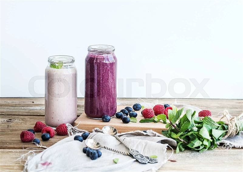 Fresh healthy smoothie with blueberries, raspberries in glass jars and mint over rustic wood background, stock photo