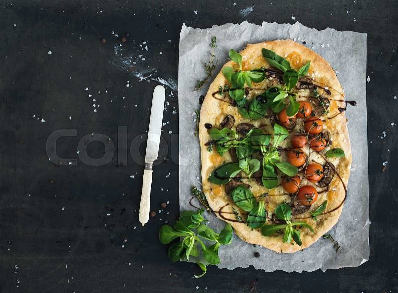 Rustic homemade pizza with fresh lamb\'s lettuce, mushrooms and cherry-tomatoes over dark grunge background, top view, copy space, stock photo