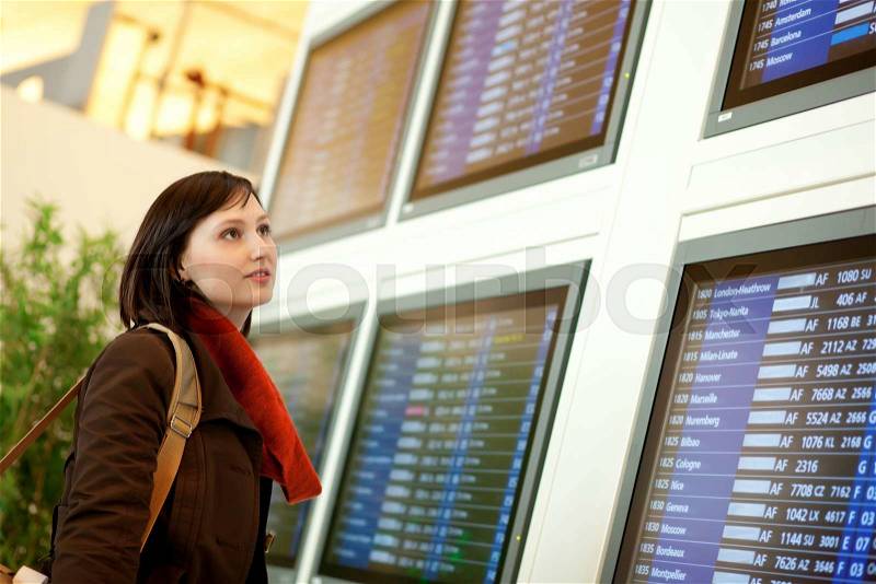 Beautiful young tourist in the airport looking at the flight board, stock photo