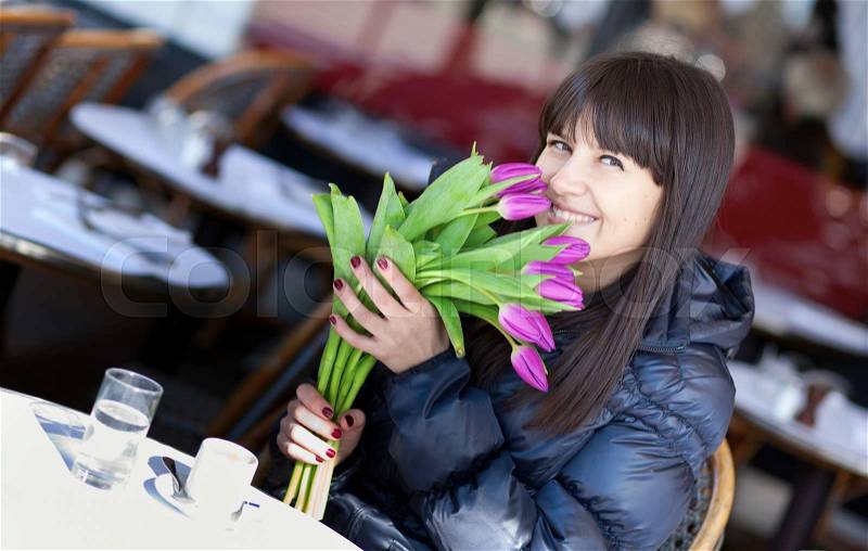Smiling brunette lady with beautiful tulips in Parisian street cafe, stock photo