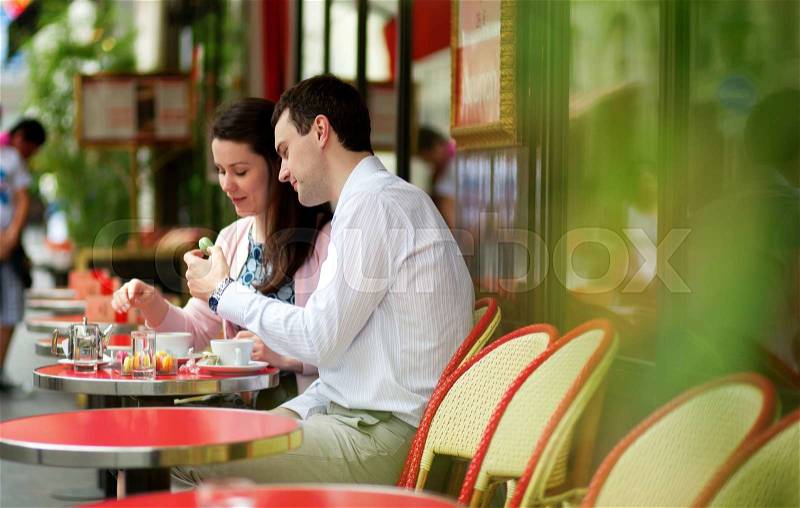 Happy couple eating macaroons in a Parisian outdoor cafe, stock photo