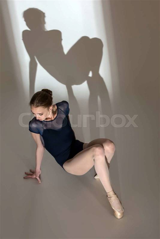 Full-length portrait sitting on the floor of a graceful ballerina in a studio on a white background. Dancer in a blue bathing suit. Against the background of her beautiful shadow, stock photo