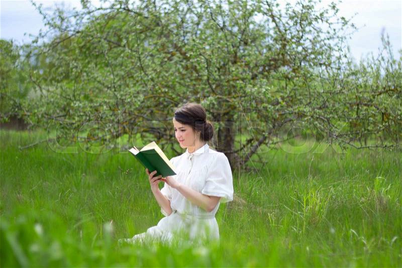 Portrait of young beautiful woman sitting with book on summer meadow, stock photo