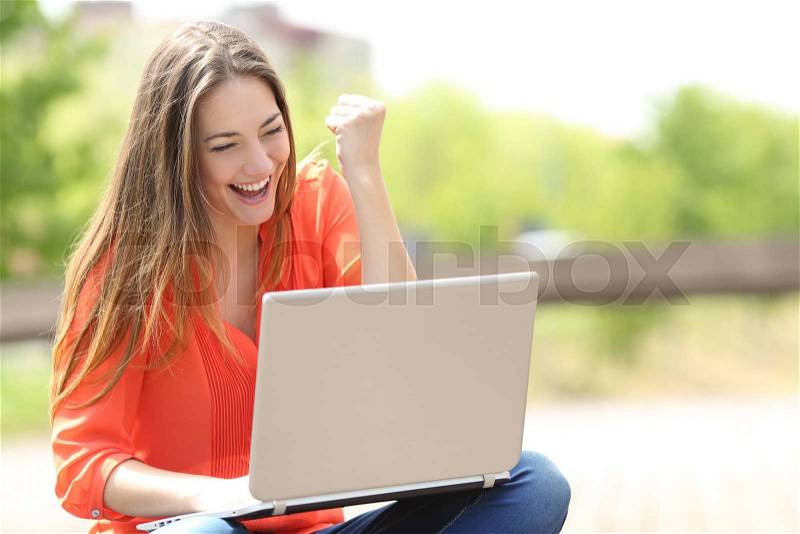 Euphoric woman searching job with a laptop in an urban park in summer, stock photo