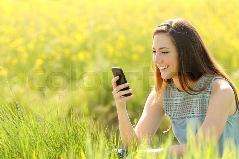 Woman using a smart phone in a green field with yellow flowers in summer, stock photo