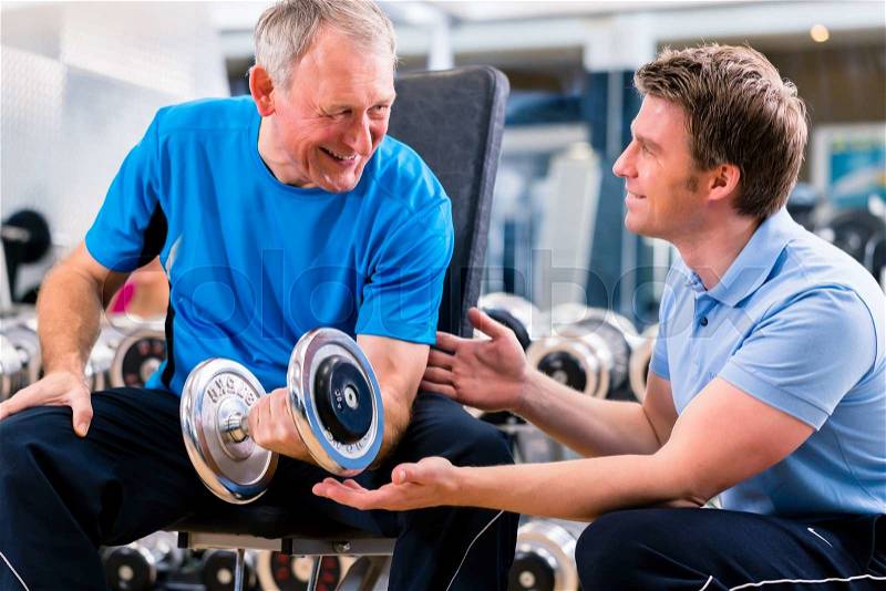 Senior man and trainer at exercise in gym with dumbbell weights, stock photo