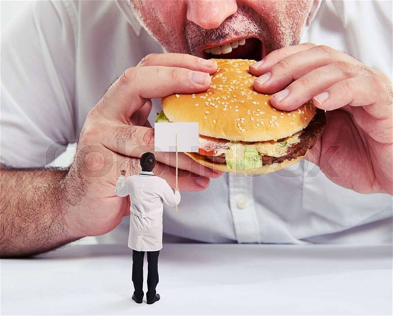 Close up photo of man eating burger with french fries and small doctor looking at him and protesting against junk food, stock photo