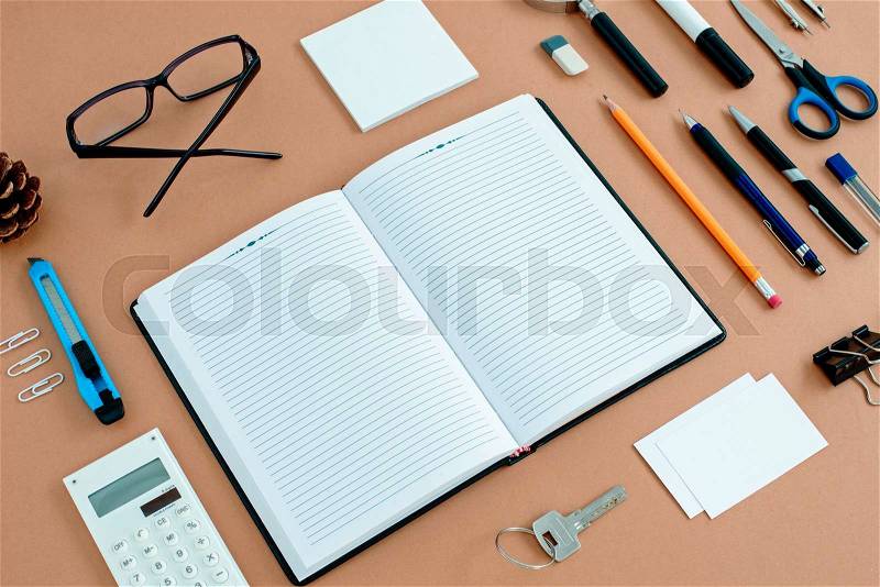 Assortment of Office Supplies Neatly Organized Around Note Book Open to Blank Page on Desk Top Surface, stock photo