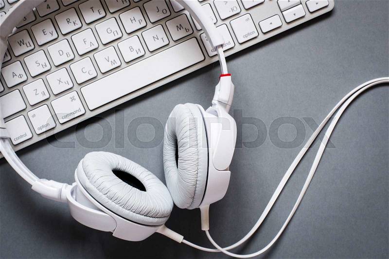 High Angle View of Modern White Audio Headphones with Cord and Computer Keyboard on Grey Desk Background, stock photo