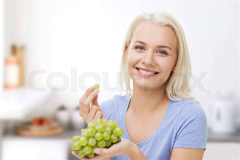 Healthy eating, food, fruits, diet and people concept - happy woman eating grapes over kitchen background, stock photo