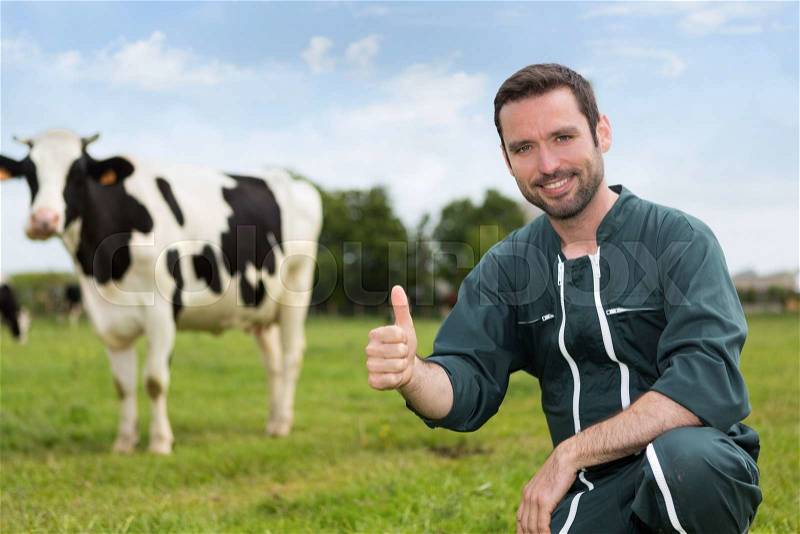Portrait of a young attractive farmer in a pasture with cows, stock photo