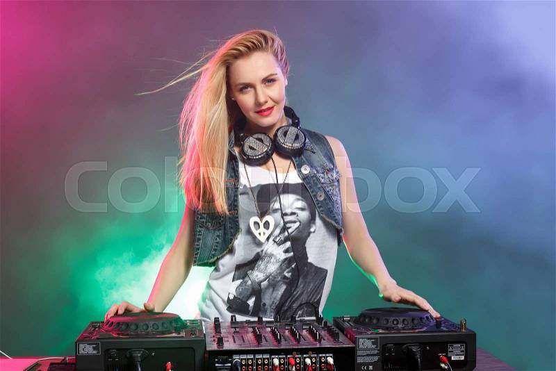 Beautiful blonde DJ girl on decks on the party on the background of multicolored smoke, stock photo