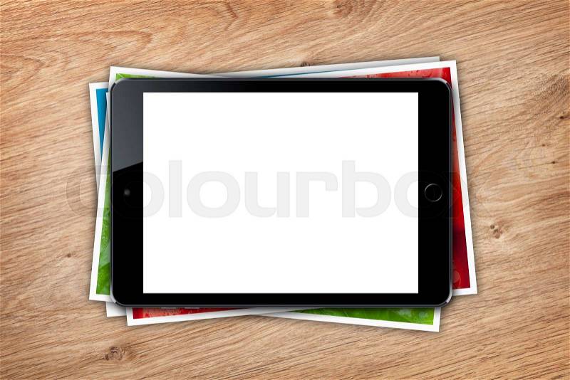 Tablet with blank screen and stack of printed pictures collage on wooden table, stock photo