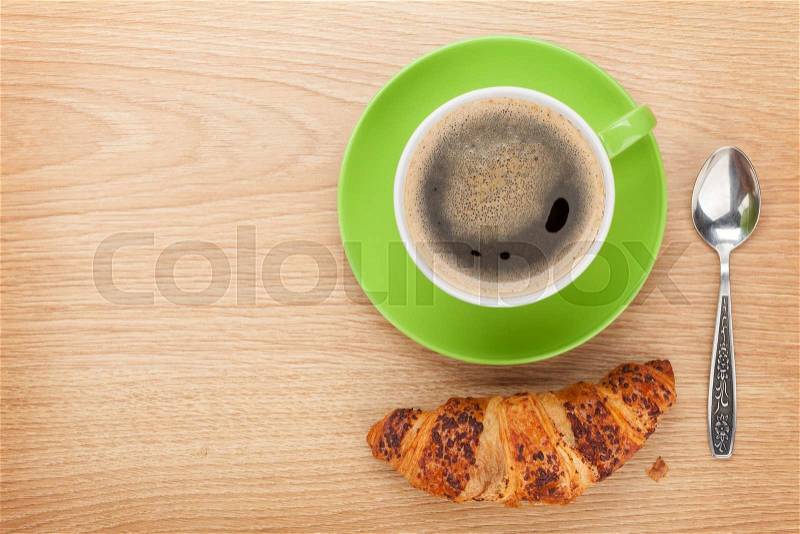 Cup of coffee and fresh croissant on wooden table with copy space, stock photo