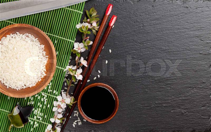 Japanese sushi chopsticks, soy sauce bowl, rice and sakura blossom on black stone background. Top view with copy space, stock photo