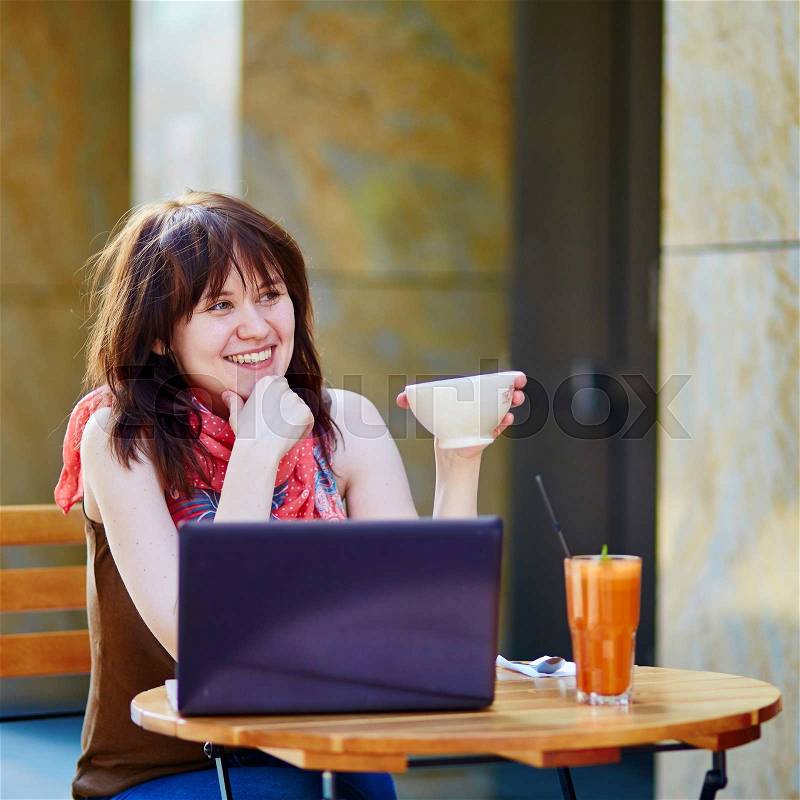 Beautiful young girl working or studying in cafe and drinking hot beverage, stock photo