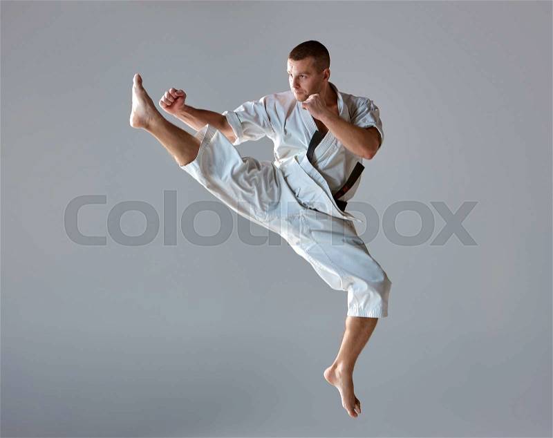Man in white kimono and black belt training karate over gray background, stock photo