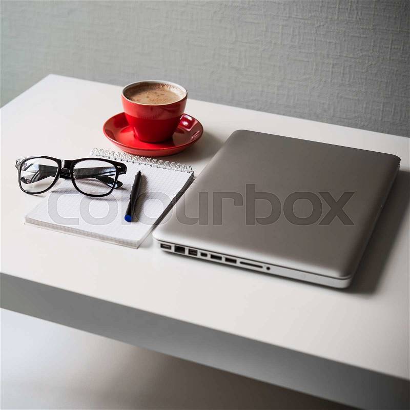White office table on which laptop, red cup of coffee, glasses, notebook and pen, stock photo