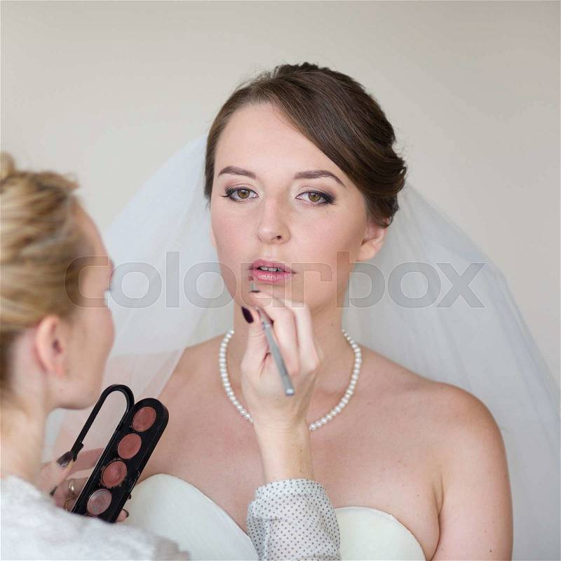 Stylist making up young beautiful bride before wedding, stock photo