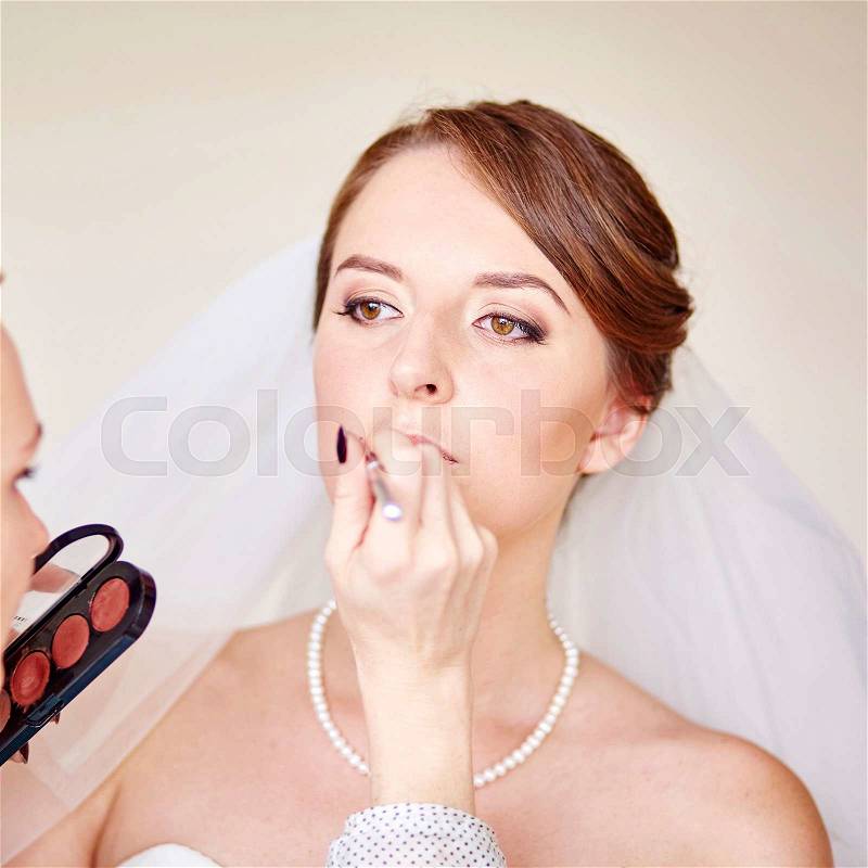Stylist making up young beautiful bride before wedding , stock photo